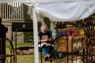 A woman waits outside her tent for customers. To pass the time she crochets more goods that she can put on display at her station and hopefully sell. 